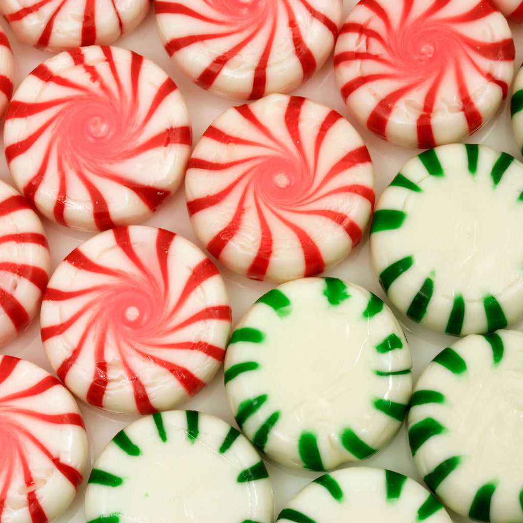 Close-up of peppermint hard candies showing red swirls and green-striped white mints on a white background
