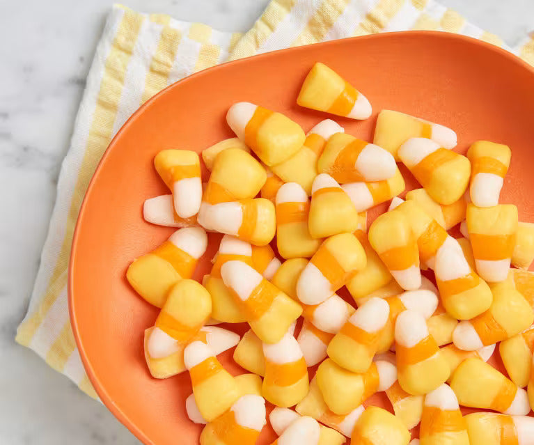 Overhead view of candy corn in an orange bowl showing classic white, orange, and yellow pieces on a marble surface