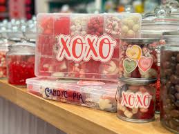 Assorted Valentine’s Day candies in clear jars and boxes, including a container labeled XOXO, on a shop counter