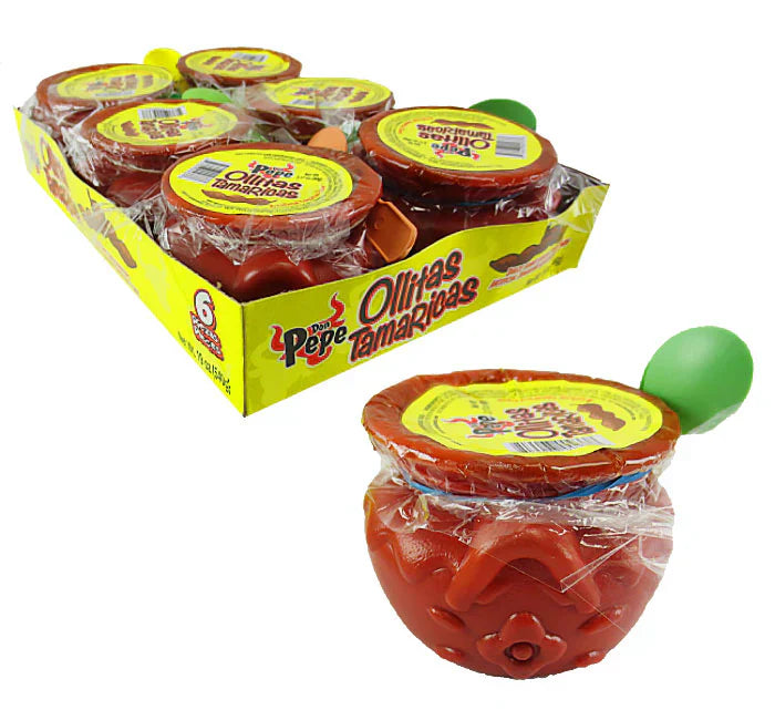 Angled view of Ollitas Tamarindas tamarind candy cup with plastic peel-off lid and green scoop beside a six-pack display tray