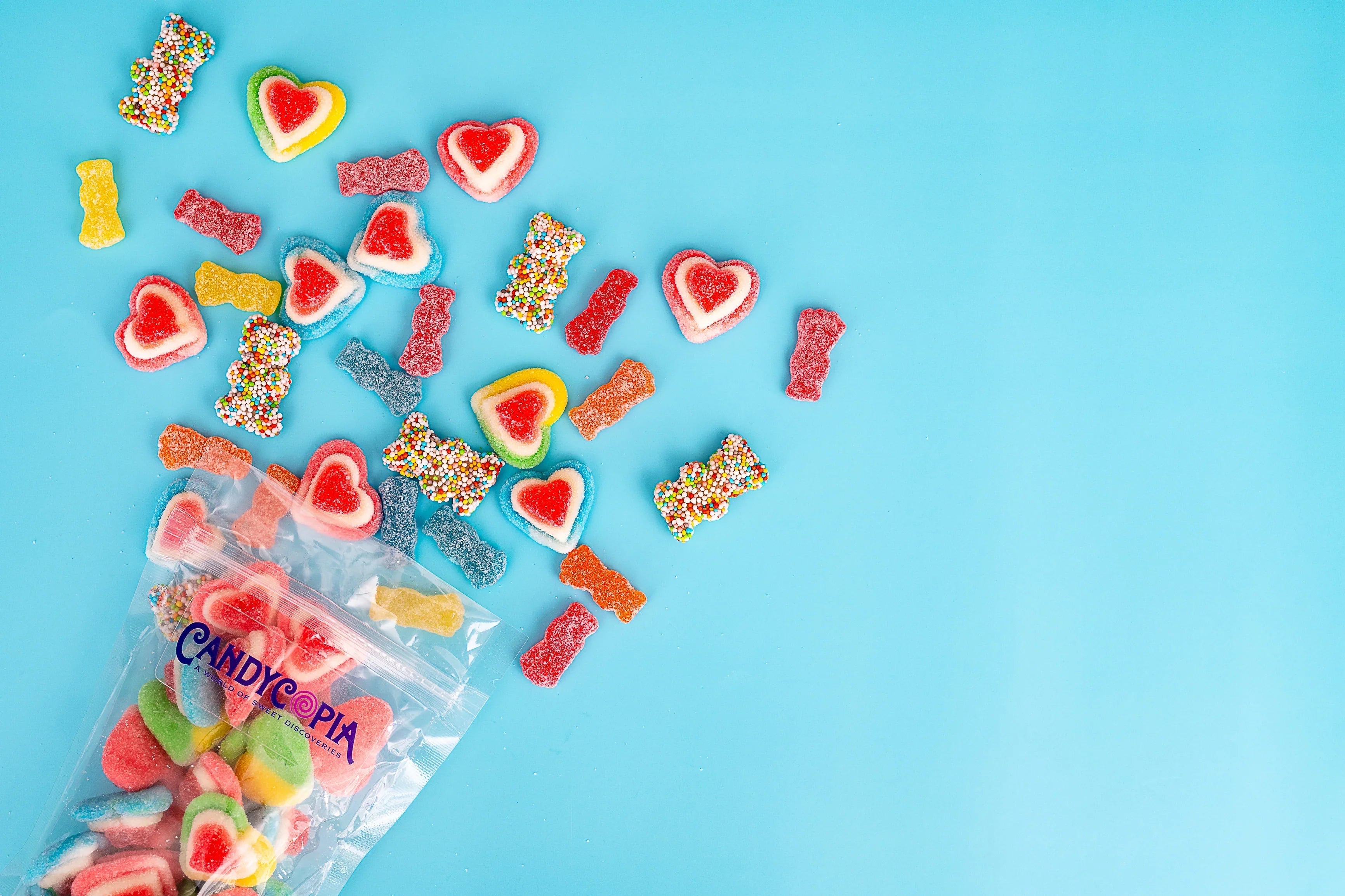 Assorted colorful gummy candies spilling from a Candycopia pick-and-mix bag on a bright blue background