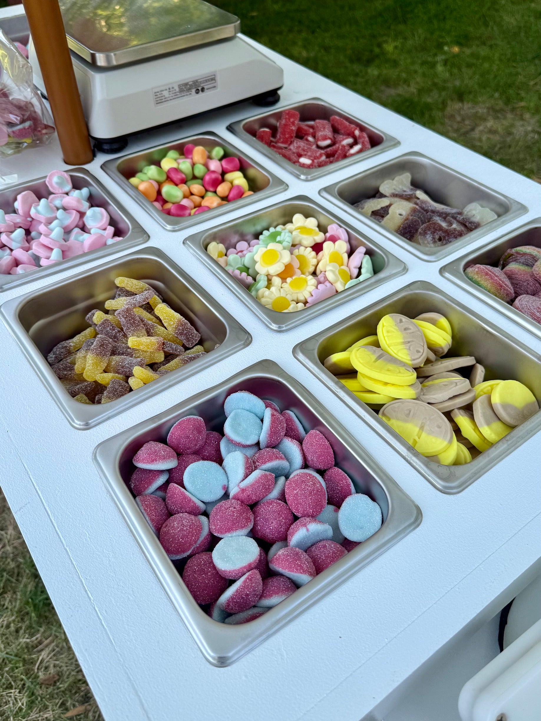 Top-down view of Mobile Swedish Candy Cart showing stainless-steel bins of assorted Swedish candies on a white cart outdoors