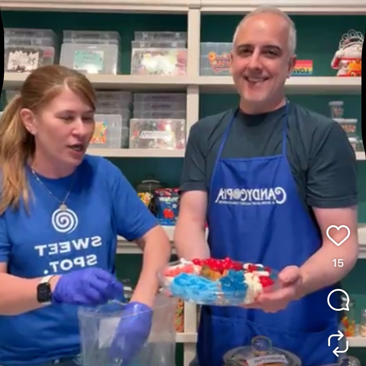 Two Candycopia employees in blue aprons and gloves actively filling a candy platter in a store setting